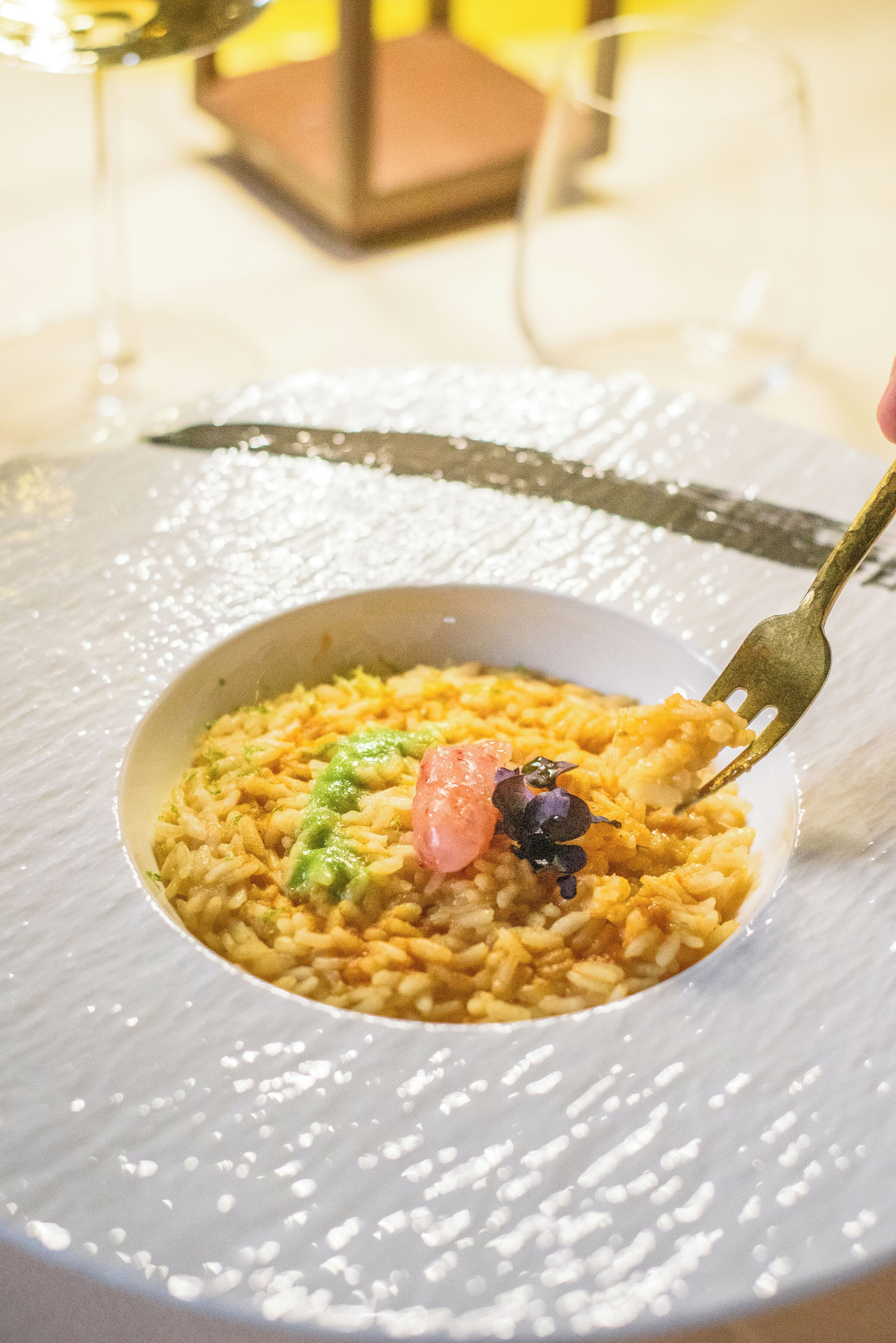 Un tazón de arroz con salsa verde y una guarnición rosada sobre un plato blanco con textura.