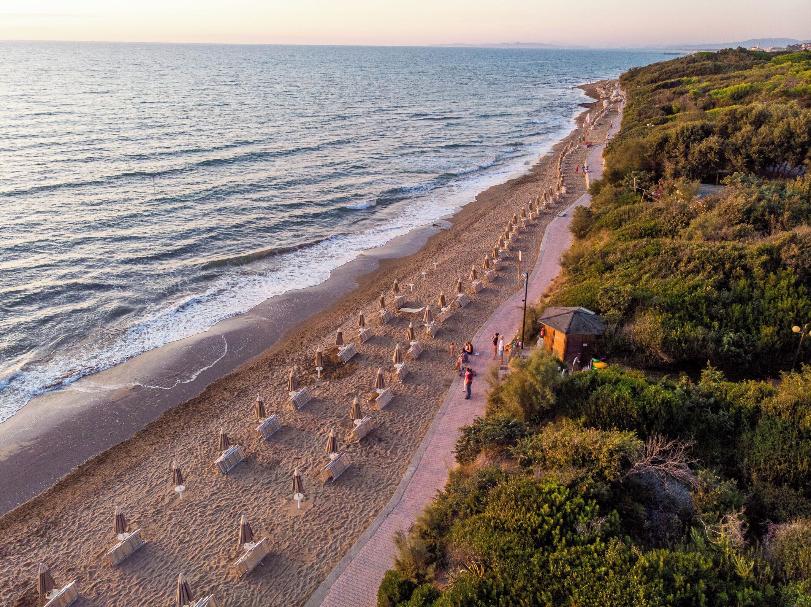 A beach with rows of umbrellas and a pathway along the shore.