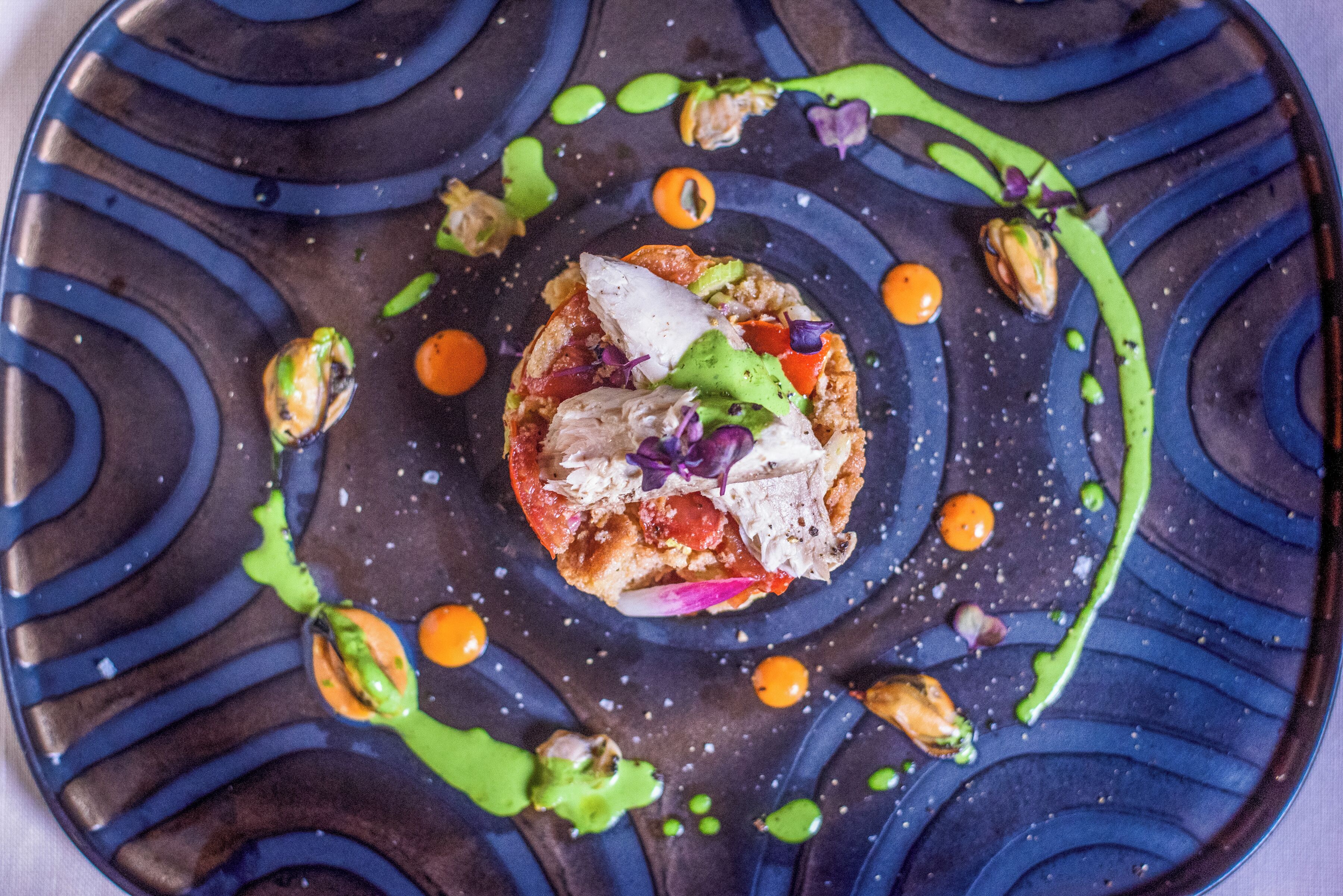 A plate with a central food item surrounded by green sauce and small orange spheres.