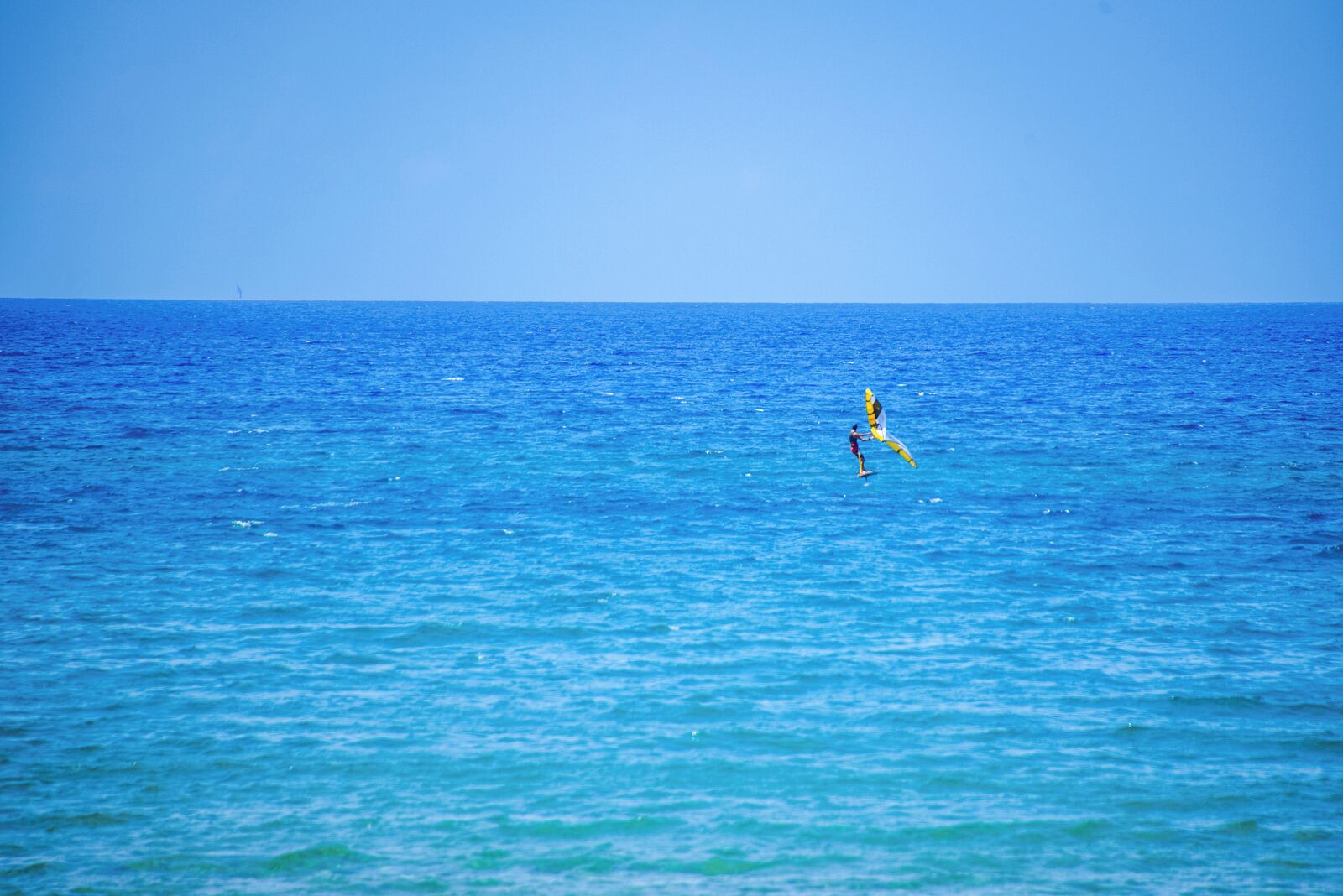 A clear view of the ocean with a person windsurfing.