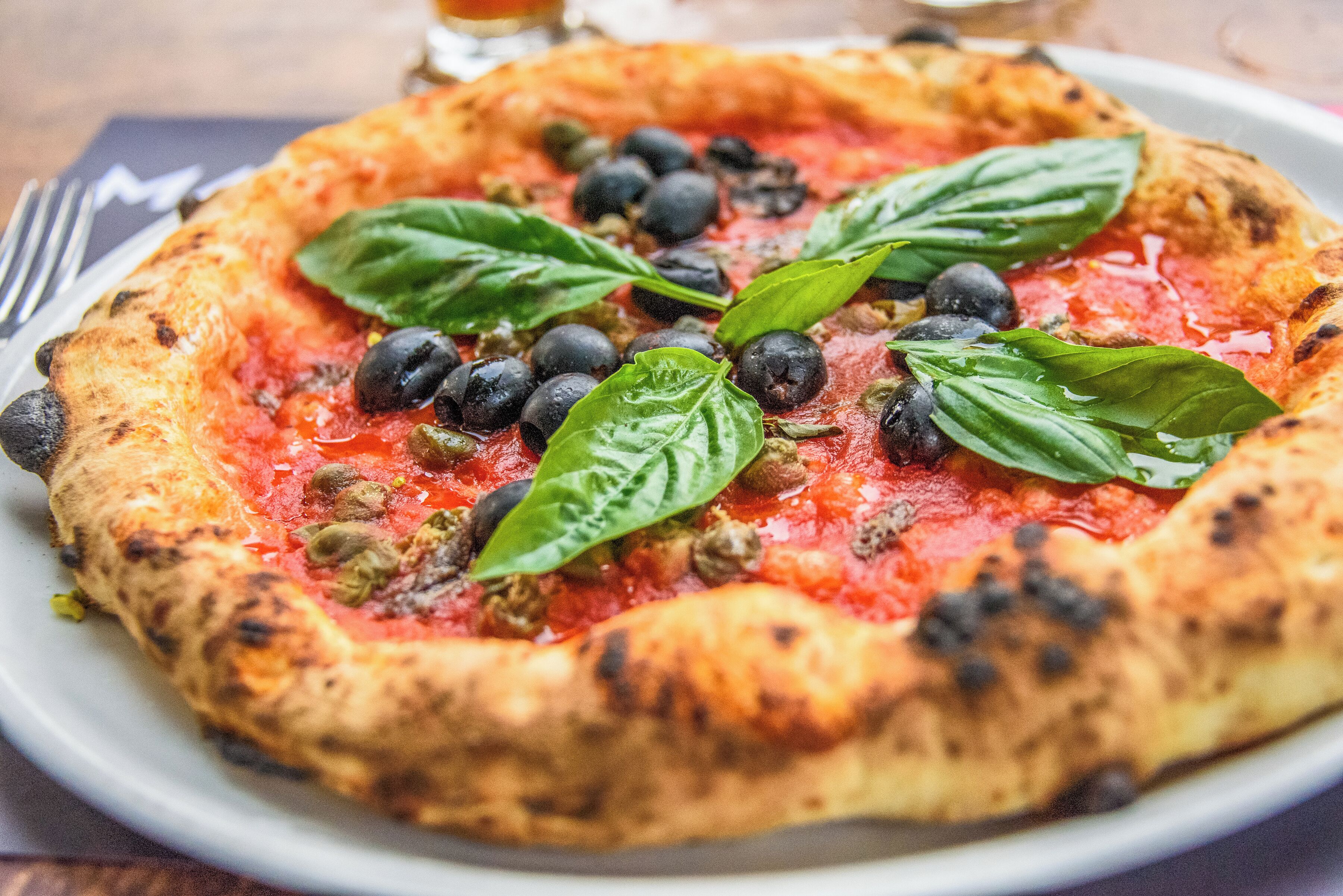 Pizza con aceitunas negras, hojas verdes y corteza quemada.