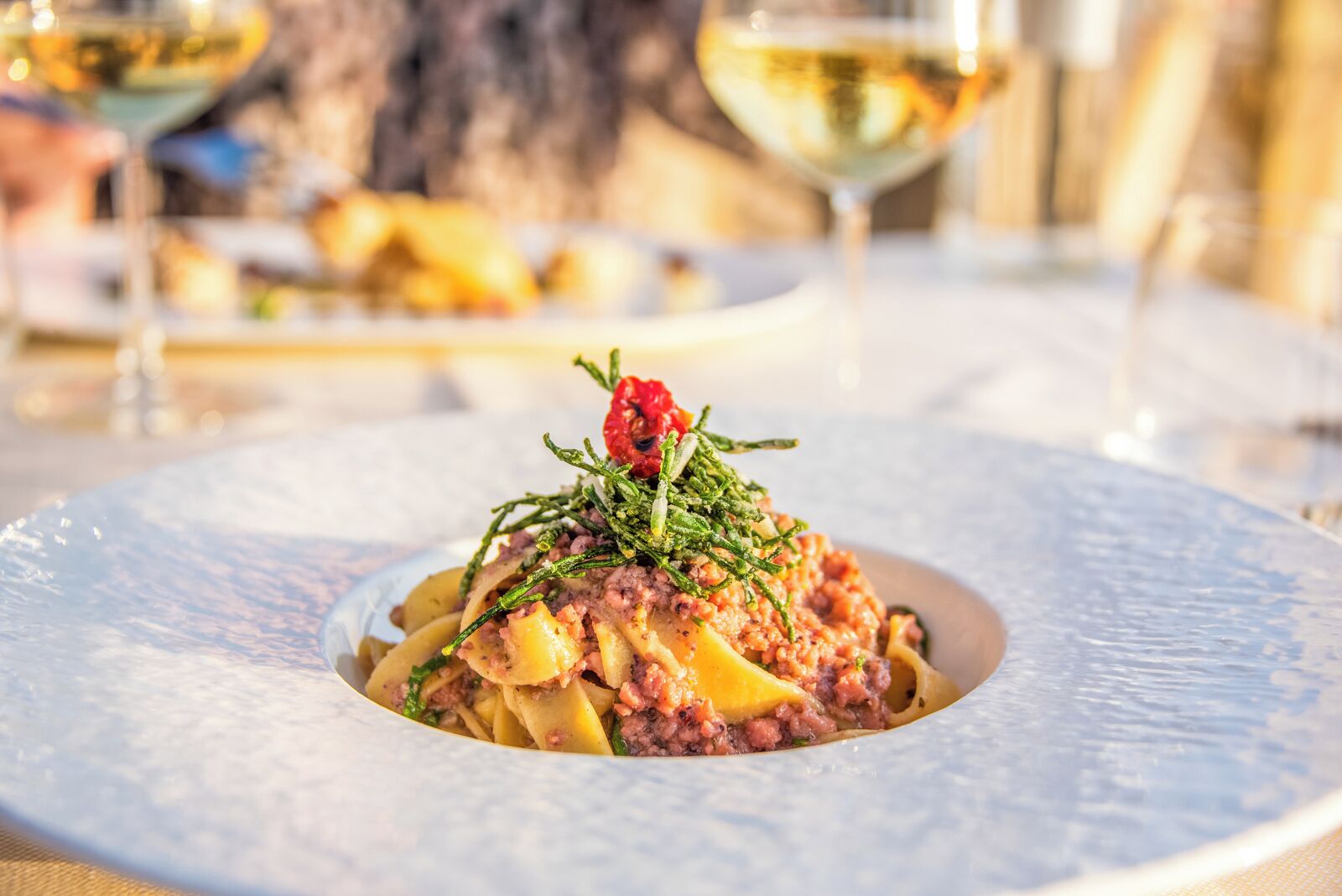 A plated dish with pasta, meat, and garnishes, set on a table with a blurred background.