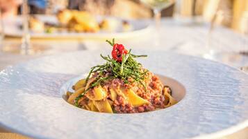 Ein angerichtetes Gericht mit Pasta, Fleisch und Garnitur, serviert auf einem Tisch mit unscharfem Hintergrund.