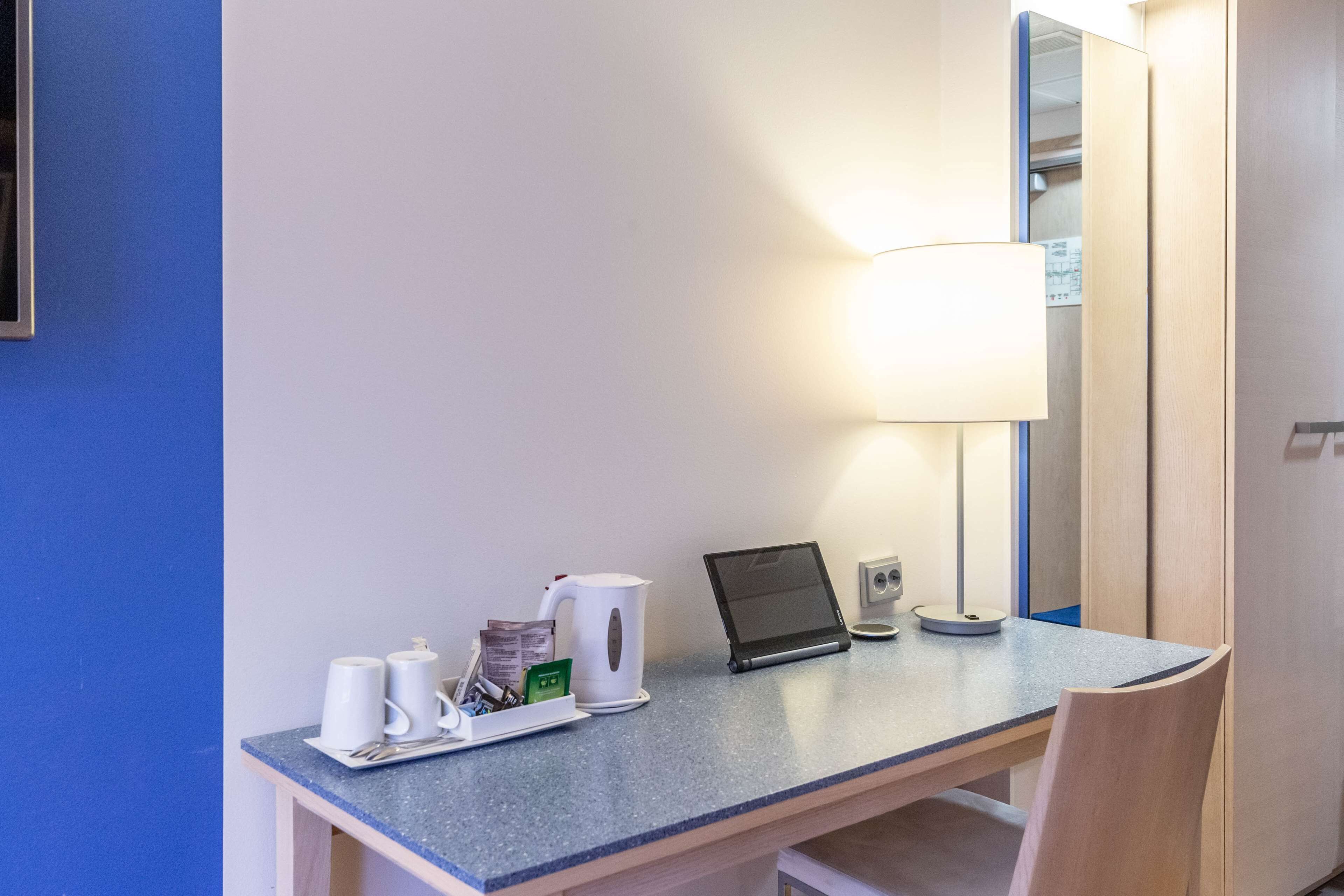 Een hotelkamer met een bureau, een laptop, een lamp en een koffiezetapparaat.
