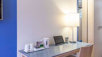 Een hotelkamer met een bureau, een laptop, een lamp en een koffiezetapparaat.