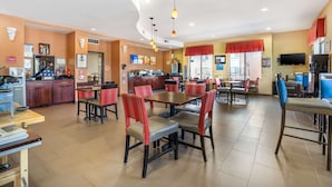Een ruim restaurant met meerdere eettafels en stoelen, een keukenhoek en een aan de muur bevestigde televisie.