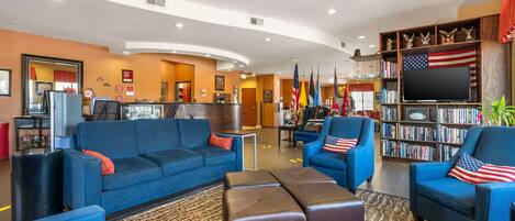 A hotel lobby with a blue sofa, armchairs, a flat-screen TV, and a bookshelf with books and flags.
