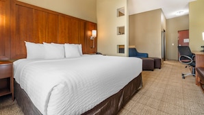 Een hotelkamer met een groot bed, een houten hoofdbord, een bureau met stoel en een klein zithoekje.