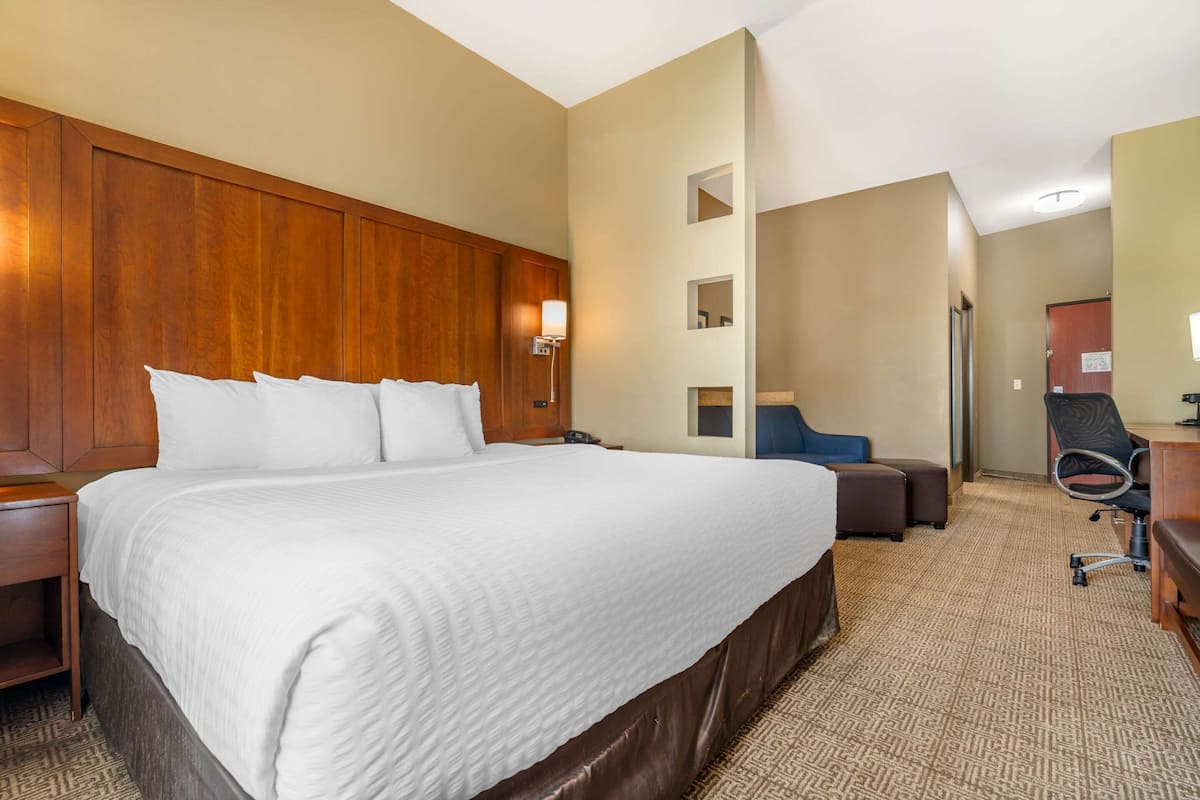 Habitación de hotel con una cama grande, cabecera de madera, un escritorio con silla y un pequeño rincón de descanso.