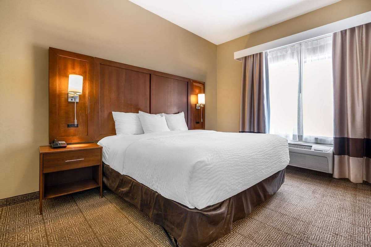Una habitación de hotel con una cama grande, un cabecero de madera, lámparas de noche, una mesita de noche y una ventana con cortinas.
