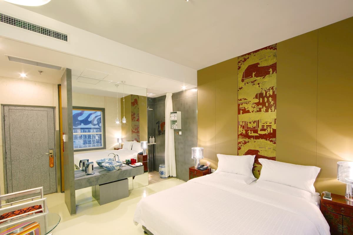A hotel room with a large bed, a bathroom with a shower, and a vanity with a sink and mirror.