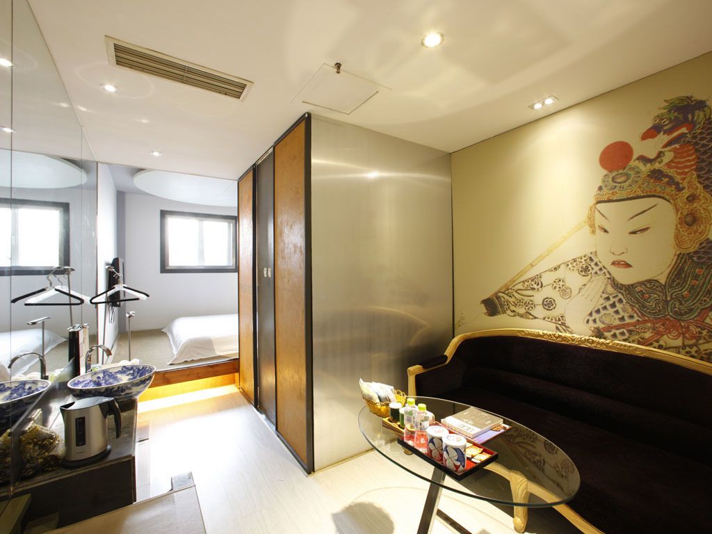 Ett modernt hotellrum med en stor säng, ett soffbord i glas, en soffa och en traditionell japansk målning på väggen.
