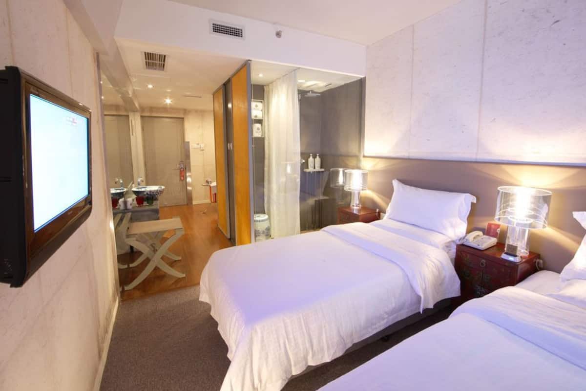 A hotel room with two beds, a desk, a mirror, and a television.