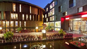 A modern building with a curved facade, large windows, and a reflective water feature in the foreground. - China Community Art Habitat Hotel (Qingdao)