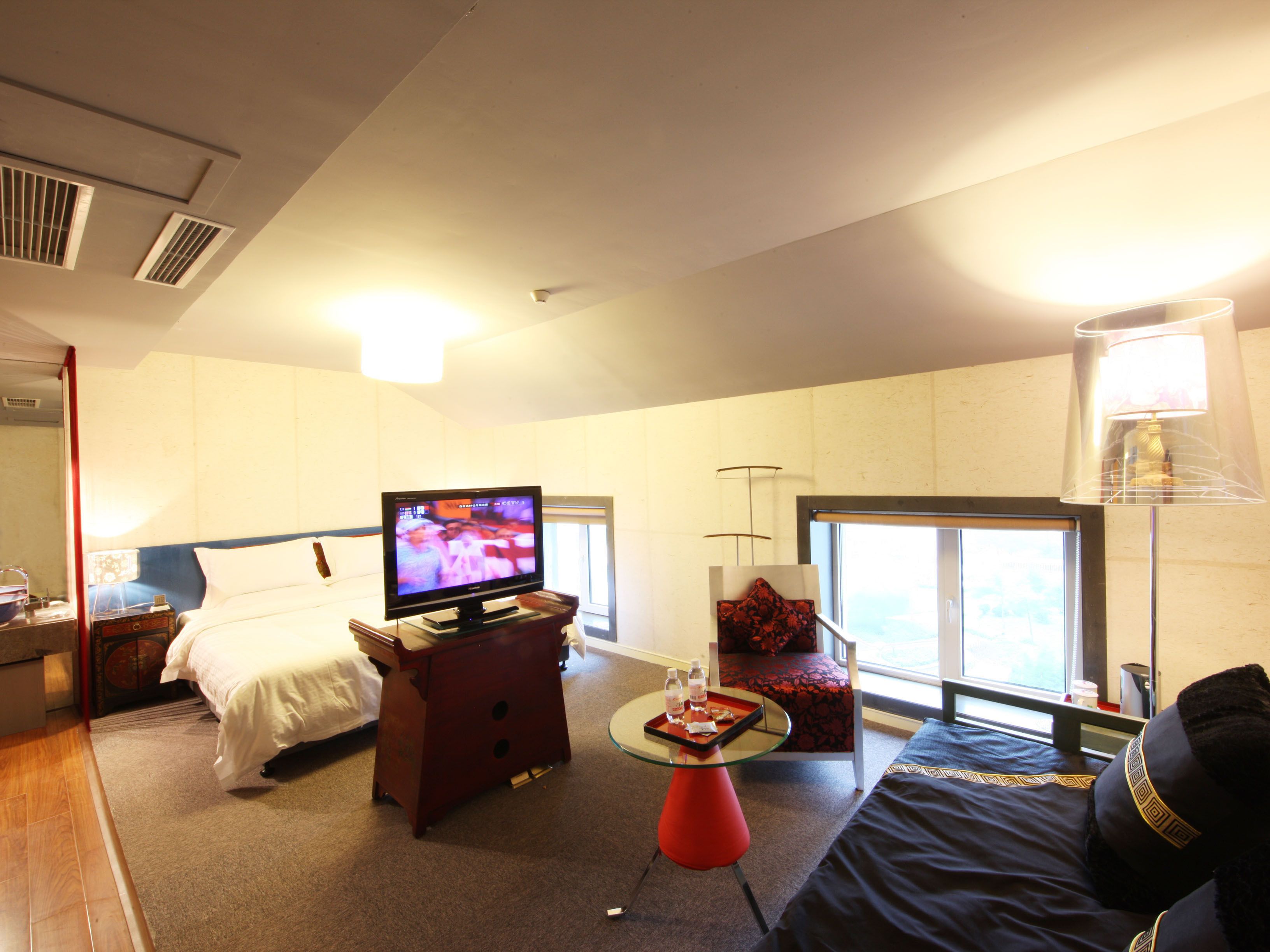 Ein Hotelzimmer mit Bett, Fernseher, kleinem Tisch mit Tablett, Stuhl und Fenster mit Aussicht.