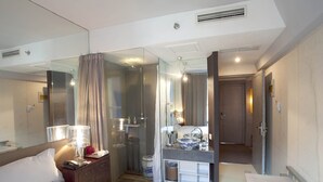 A hotel room with a bed, a desk with a mirror, a shower area, and a bathroom. - China Community Art Habitat Hotel (Qingdao)