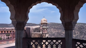 Une vue d’un bâtiment historique doté d’un dôme et d’un clocher, encadré d’arches, qui surplombe un paysage vallonné.