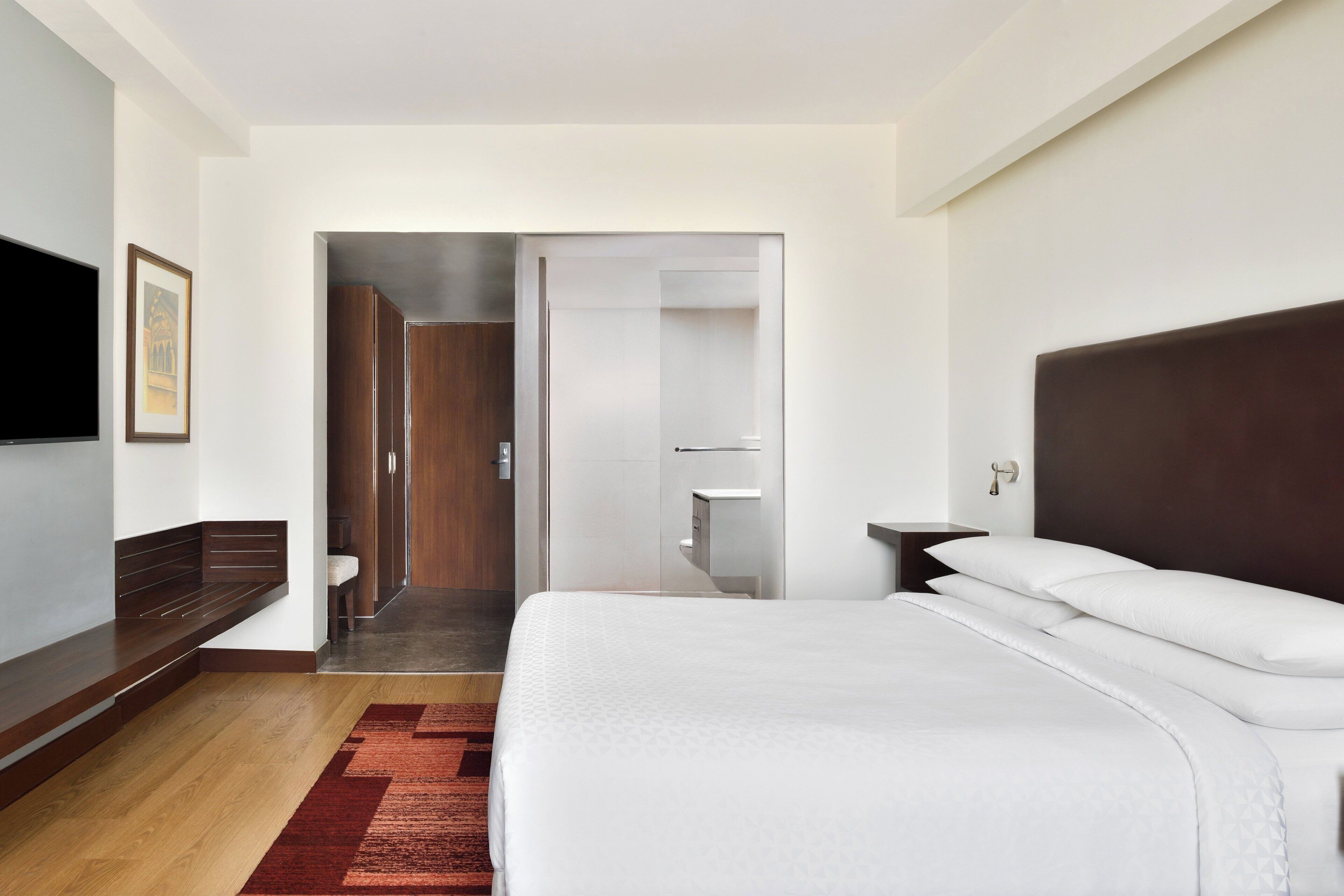 Una habitación de hotel moderna con una cama grande, un televisor de pantalla plana en la pared y un banco de madera junto a la ventana.