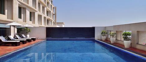 A rooftop swimming pool with lounge chairs and potted plants.