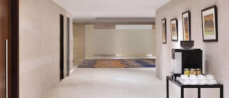 Un pasillo con suelo de baldosas, alfombra estampada, una mesa con tazas y frascos, y cuadros en la pared.