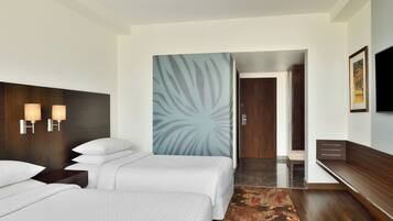 A hotel room with two beds, a large wall mural, a TV, and a wooden bench.