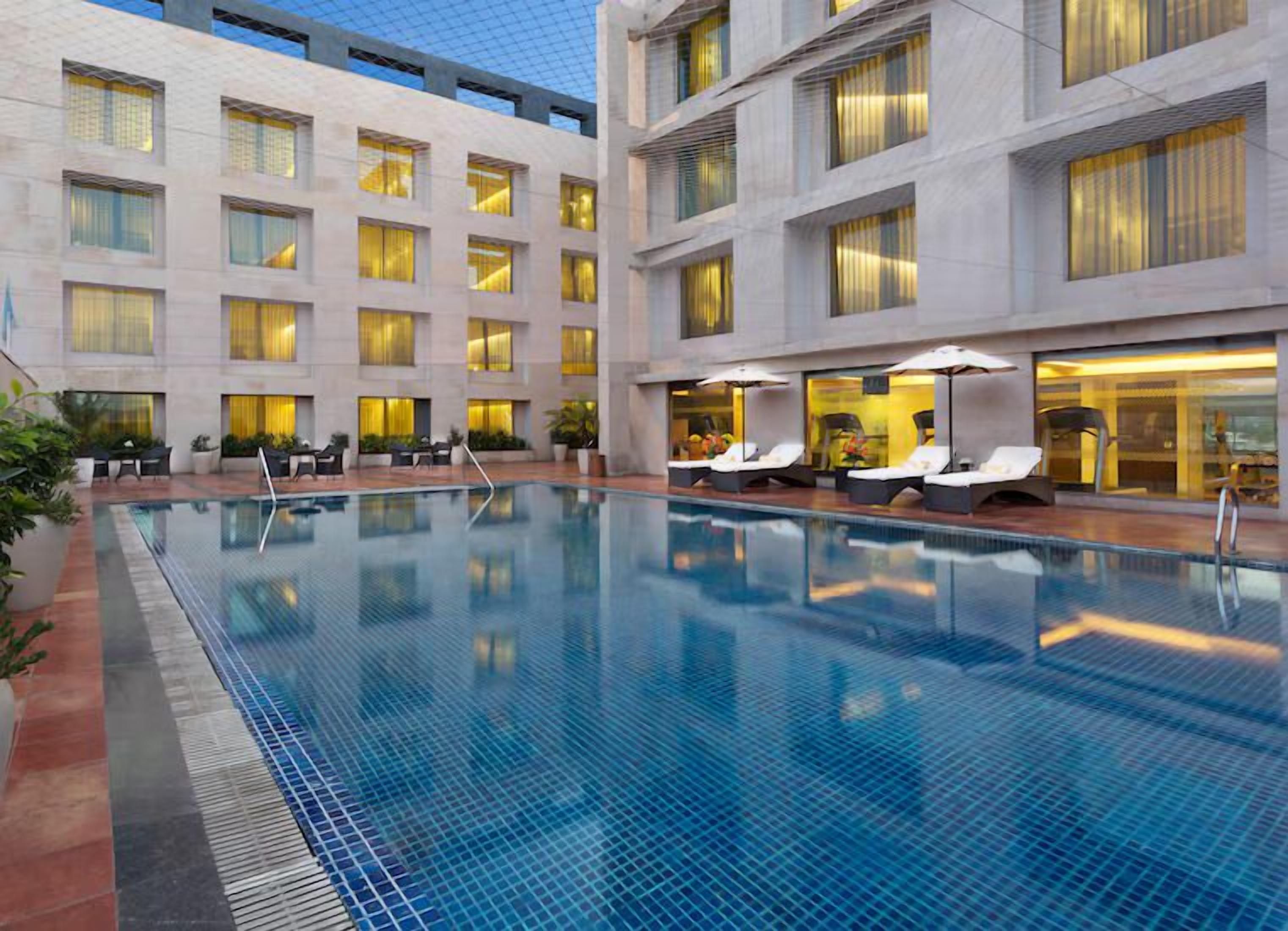A hotel pool area with lounge chairs and umbrellas, surrounded by a building with multiple floors and windows.