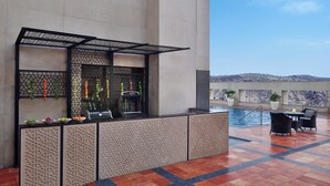 Un espace aménagé au bord de la piscine, avec un bar, des sièges et une vue sur les montagnes.
