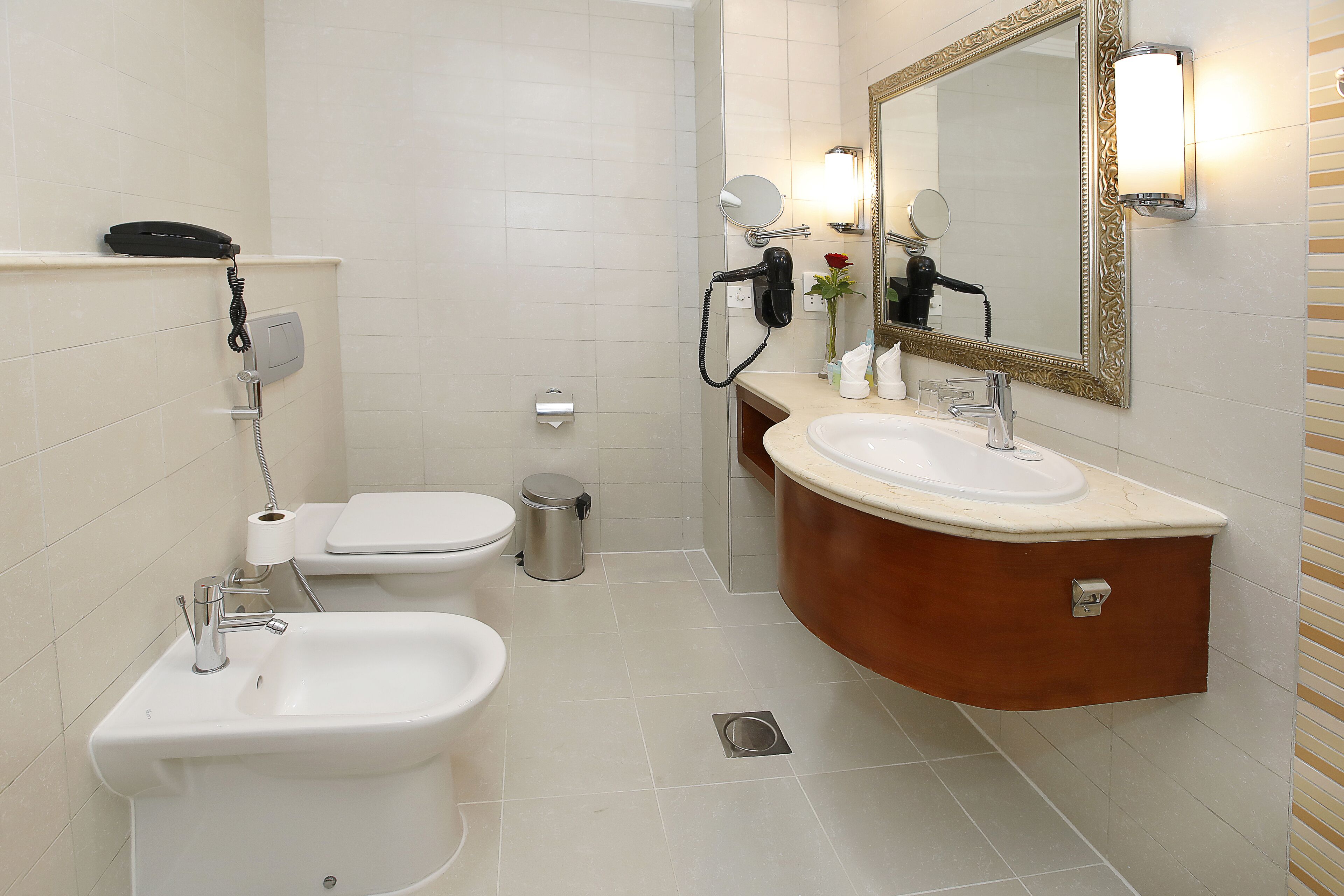 A bathroom with a sink, bidet, toilet, and a mirror with a light.