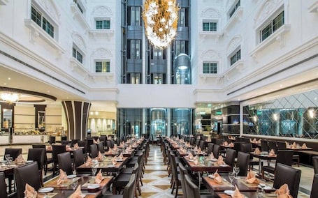 A spacious hotel lobby with multiple dining areas, a grand chandelier, and a modern glass facade.
