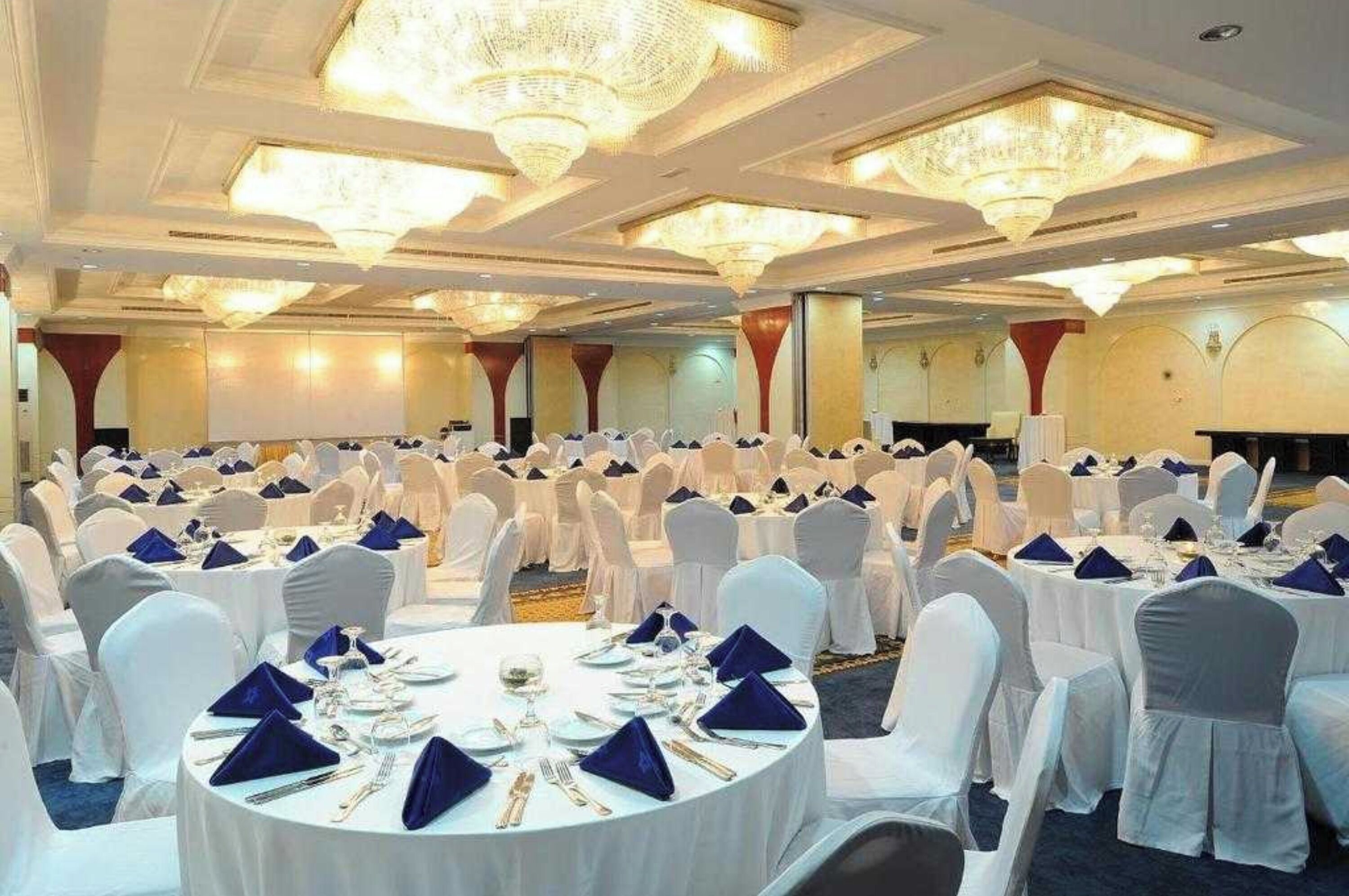 Un salón de banquetes con mesas redondas dispuestas para comer, sillas blancas y candelabros.
