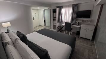 Quarto de hotel com cama, escrivaninha, cadeira, televisão e cozinha compacta.