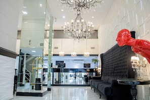 A lobby with a chandelier, a red sculpture, a sofa, and a reception desk. - Ker Recoleta Hotel (Buenos Aires)