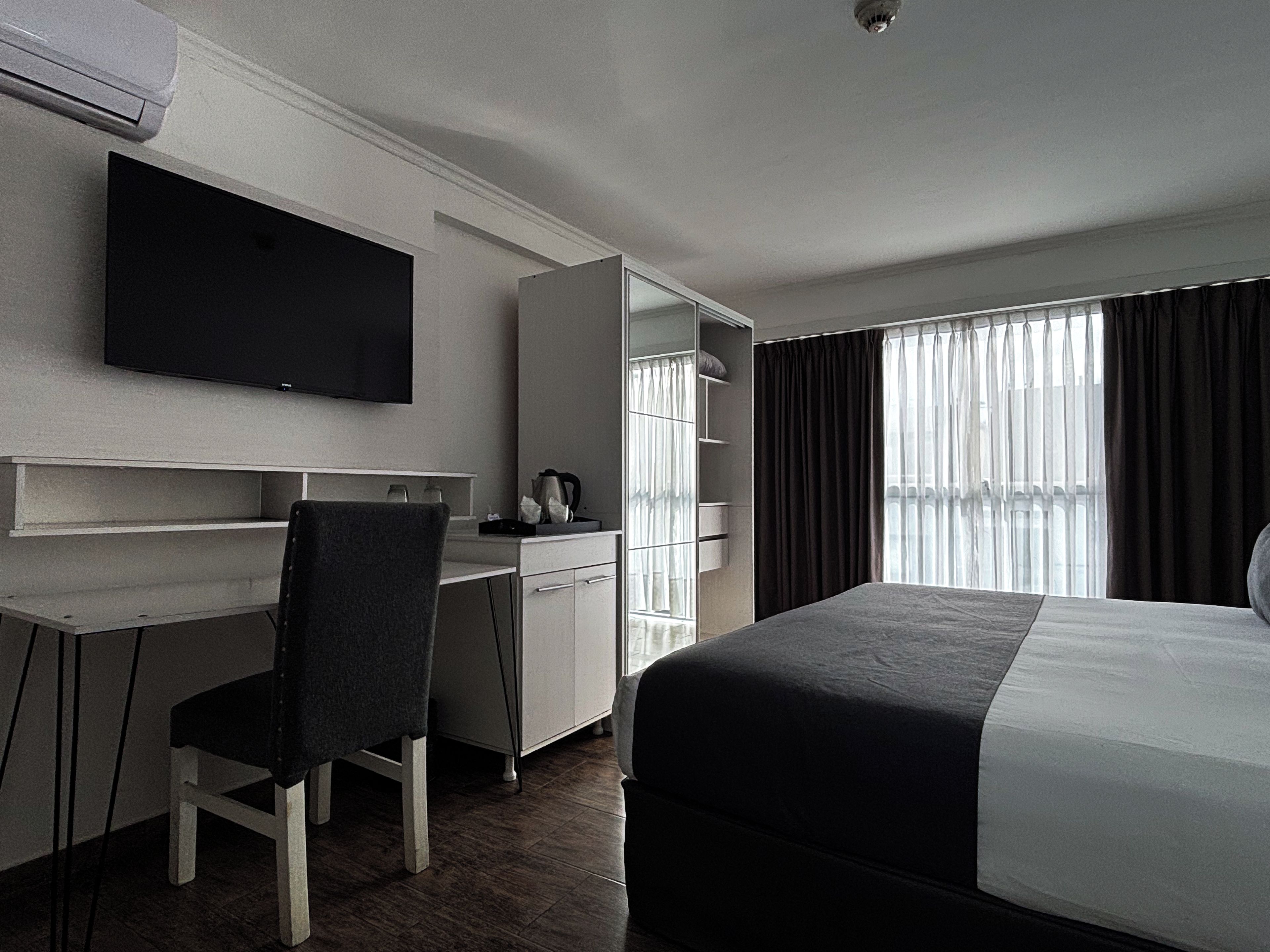 Habitación de hotel con cama, escritorio, silla, televisor y ventana con cortinas.