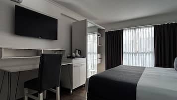 Habitación de hotel con cama, escritorio, silla, televisor y ventana con cortinas.