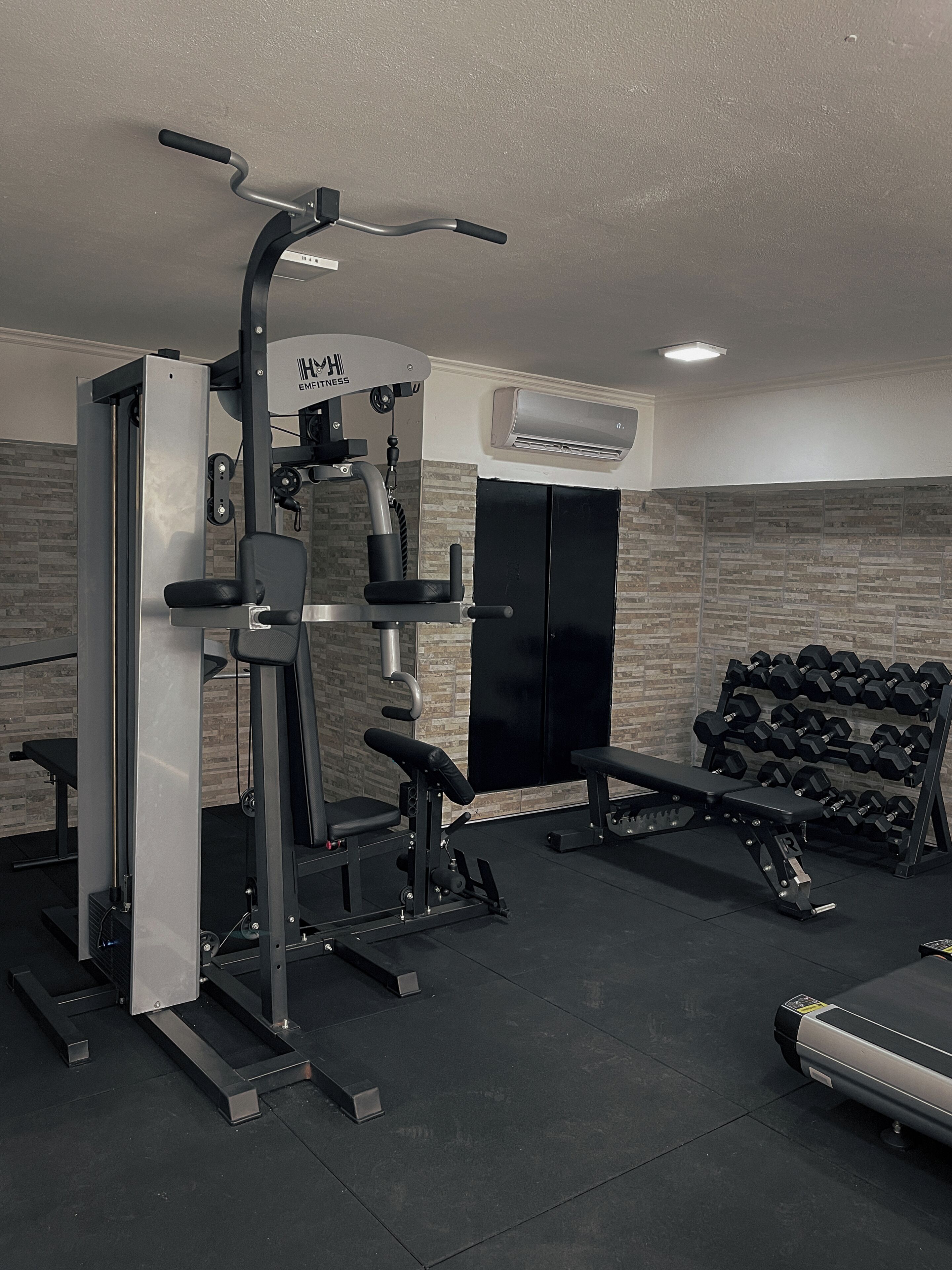 Uma academia com equipamentos de exercícios, um banco e uma estante de halteres.