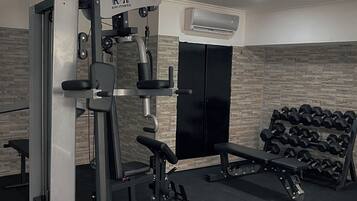 Uma academia com equipamentos de exercícios, um banco e uma estante de halteres.