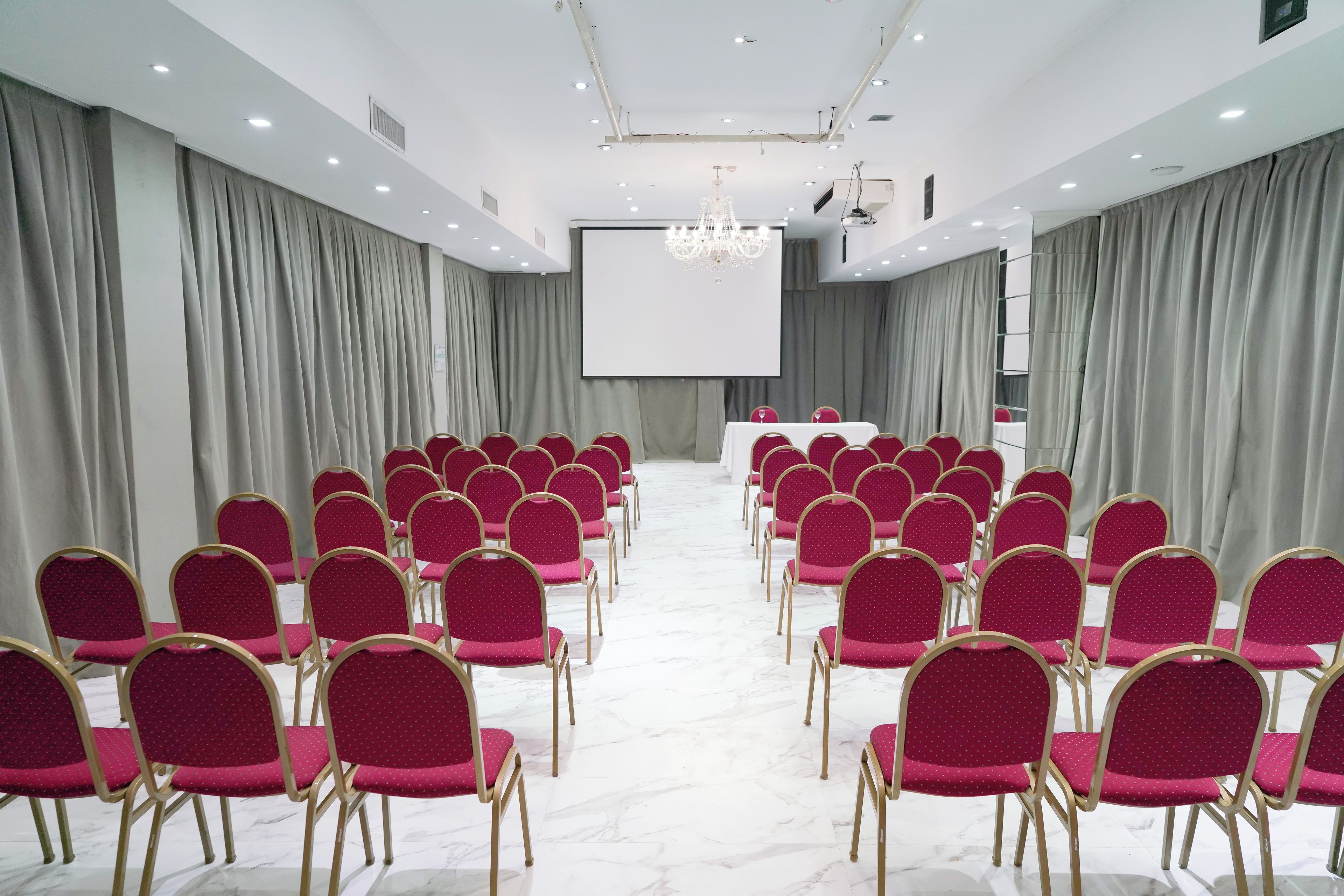 Uma sala de conferências com fileiras de cadeiras, uma tela de projeção e um pódio.