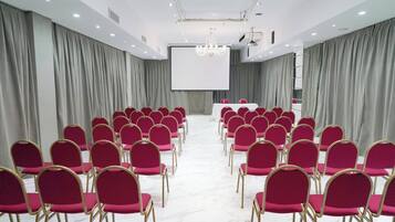 Uma sala de conferências com fileiras de cadeiras, uma tela de projeção e um pódio.