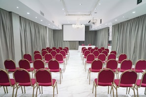 Une salle de conférence avec des rangées de chaises, un écran de projection et un pupitre.