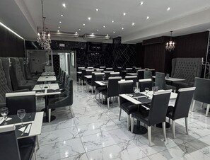 L’intérieur d’un restaurant, avec un sol en marbre, des banquettes noires recouvertes de tissu et des tables dressées pour le service.