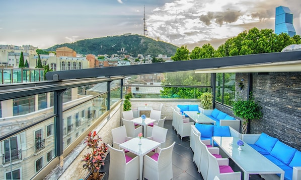 A rooftop terrace with outdoor seating, a view of the cityscape, and a mountain in the background. - River Side Hotel (Tbilisi)