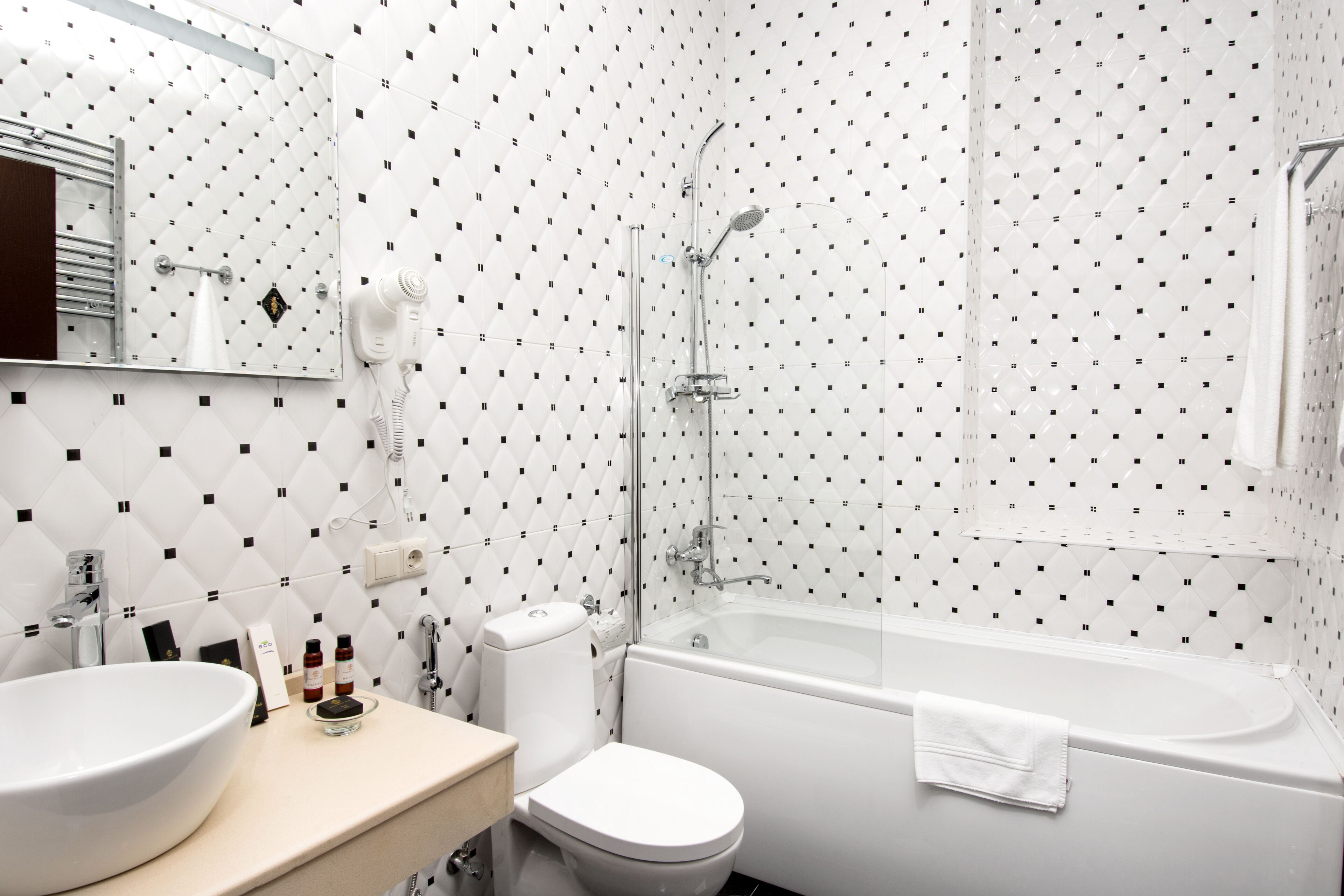 A modern bathroom with a white sink, toilet, and bathtub. There is a mirror above the sink and a showerhead above the bathtub.