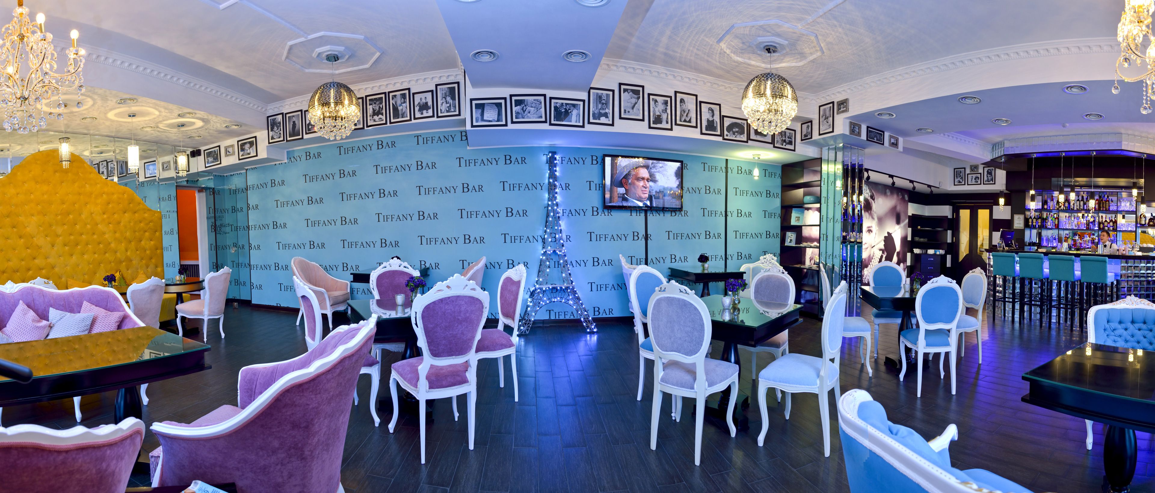A bar area with multiple seating arrangements, a television screen, and a bar counter with a variety of bottles.