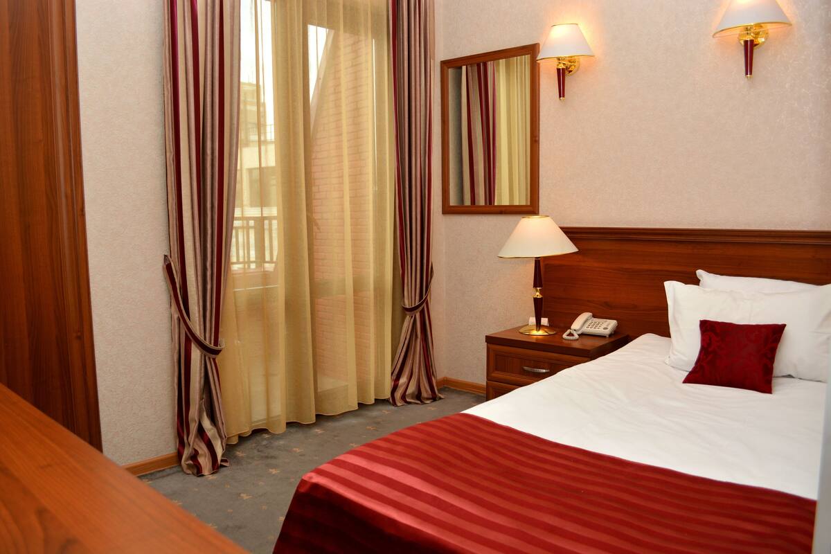 A hotel room with a bed, a nightstand, a lamp, a telephone, and a mirror.