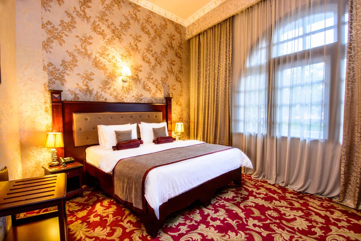 A hotel room with a large bed, a wooden headboard, a red carpet, and a window with curtains.