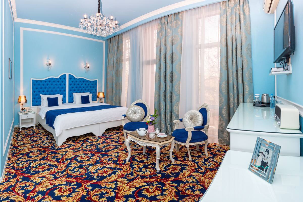 A hotel room with a large bed, a sitting area with a table and chairs, a TV, and a minibar.