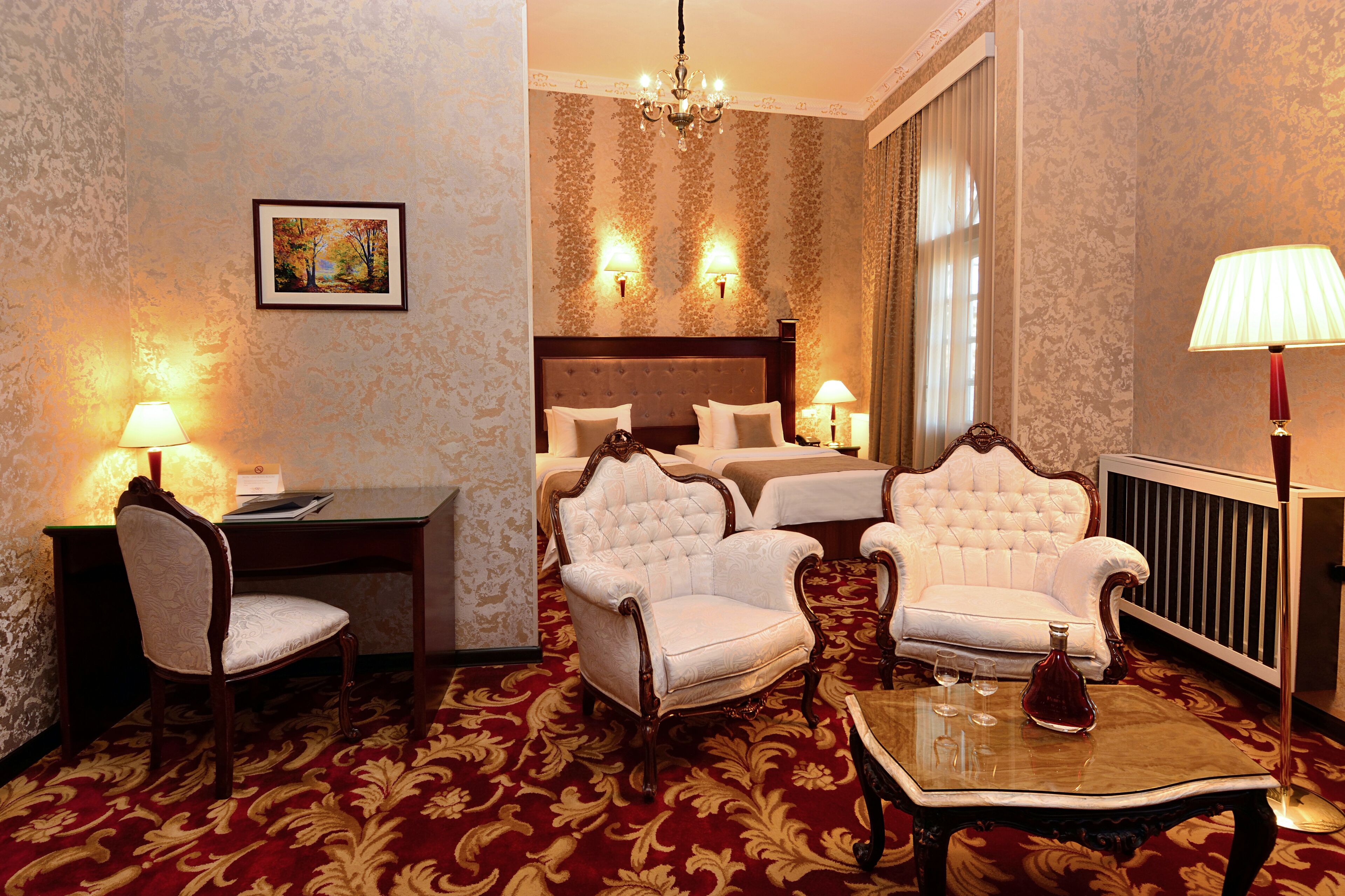 A hotel room with a large bed, two armchairs, a desk, and a table with glasses.