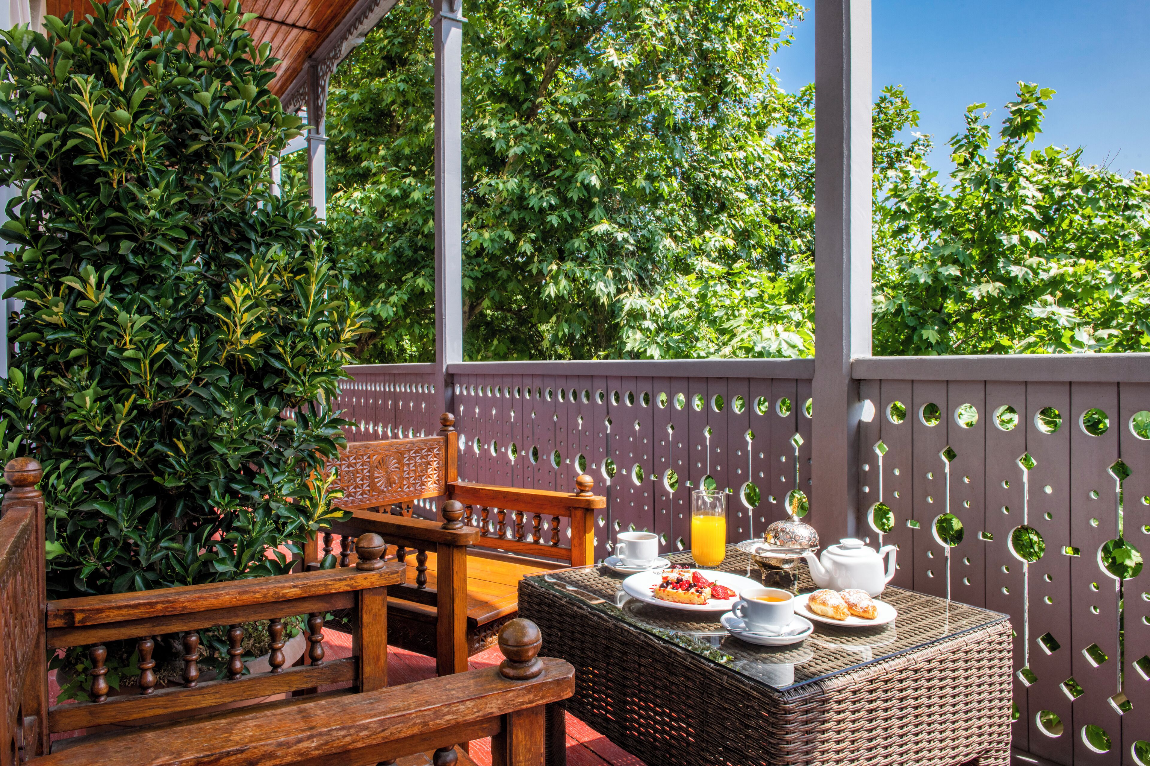 An outdoor patio with wicker furniture, a table set with breakfast items, and a decorative fence with circular cutouts.