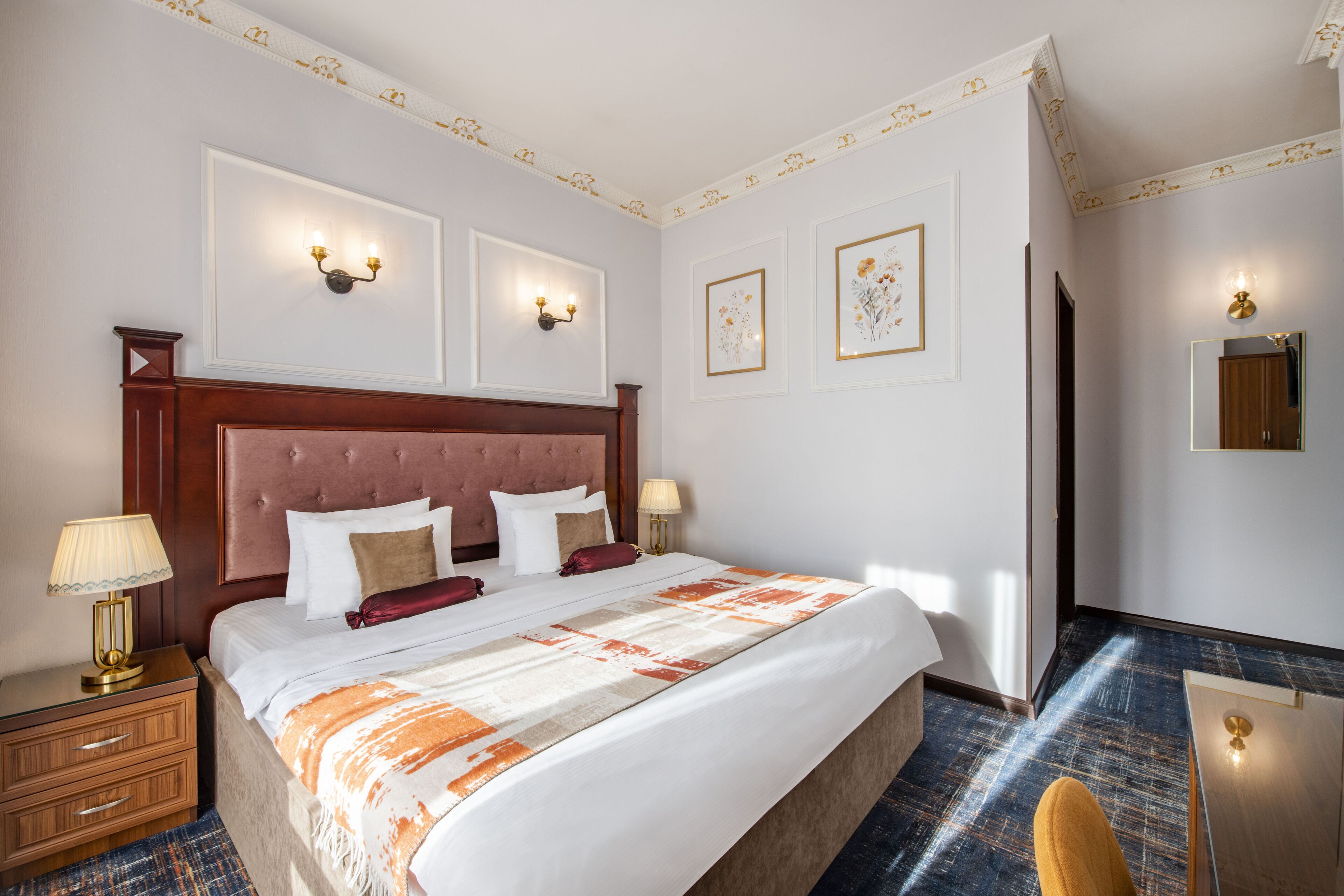 Een hotelkamer met een groot bed, twee nachtkastjes met lampen, een houten hoofdbord en kunstwerken in lijsten aan de muren.