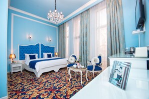 A bedroom with a large bed, a chandelier, a desk, and a chair. - River Side Hotel (Tbilisi)